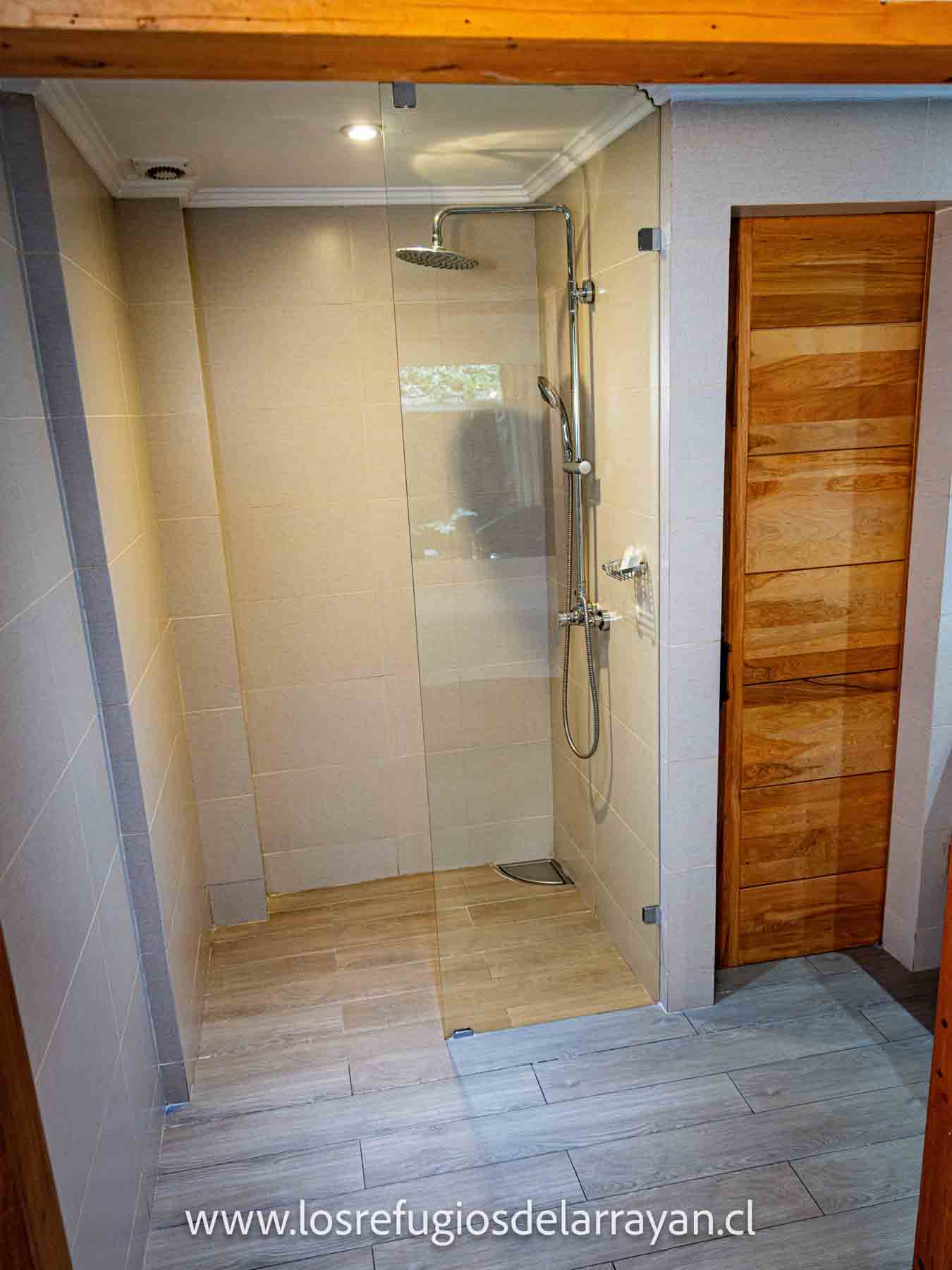Ducha moderna con puerta de vidrio y piso de madera.
